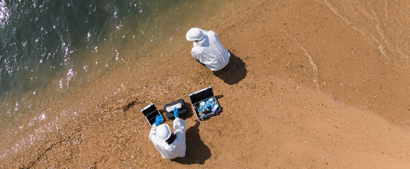 Ecologists in protective suits working near the coastline and taking samples of water for analysis