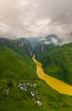 Aerial view of remote village nestled in lush valley with winding nho que river and majestic mountainous backdrop, tu san canyon, ha giang, vietnam.