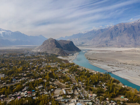 Aerial view of tranquil Indus River winding through majestic mountains and remote town, Skardu, Pakistan.
