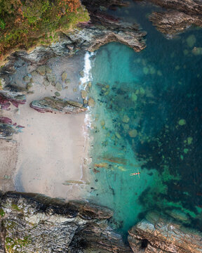 Aerial view of tranquil Lekerrock Cove with clear water and swimmer, Polperro, England.