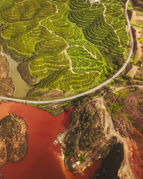 Aerial view of lush greenery and terraces with winding road and red water in mining area, Minas de Riotinto, Huelva, Spain.
