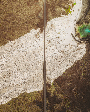 Aerial view of sandy road dividing white sand and green water at Caleta del Mojon Blanco, Orzola, Spain.