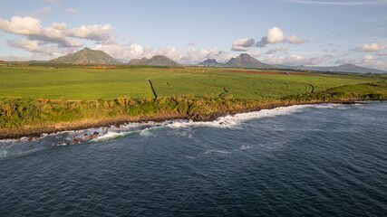 Aerial view of tranquil shoreline, green fields, and majestic mountains under a cloudy sky, Albion, Riviere Noire, Mauritius.