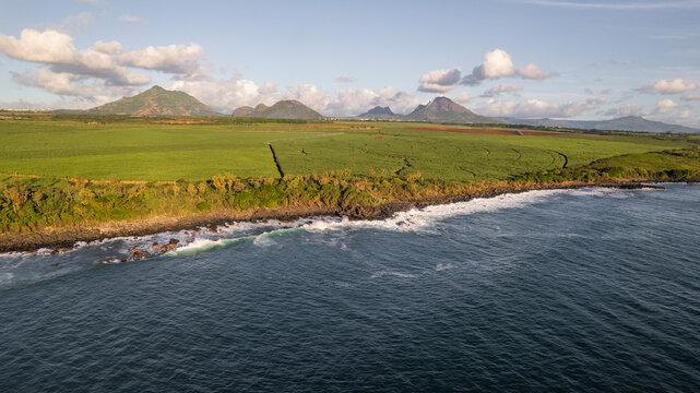 Aerial view of tranquil shoreline, green fields, and majestic mountains under a cloudy sky, Albion, Riviere Noire, Mauritius.