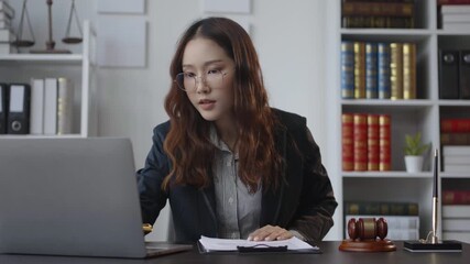 Confident businesswoman working on laptop in modern office, taking notes, and discussing business in a professional environment with legal decor and bookshelves