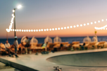 Blurred defocused background of a skate park with garland on the seashore at sunset with copy space.