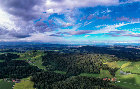 Aerial view of rolling hills, forest, and village under a serene sky, Emmental Region, Switzerland.