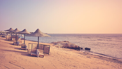 A tranquil beach with sun loungers and umbrellas at sunset, color toning applied, Marsa Alam region, Egypt.
