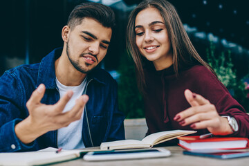 Funny hipster guy spending time with female colleague discussing ideas for project together, attractive woman student consulting with friend  checking information from notepad on cafe terrace