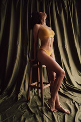 Obraz premium Full body vertical unretouched portrait of gorgeous model girl sit posing chair khaki curtain background