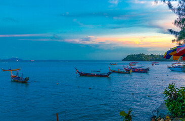 Colourful Skies Sunset over Rawai Beach in Phuket island Thailand. Lovely turquoise blue waters, lush green mountains colourful skies and beautiful views of long tail Boats