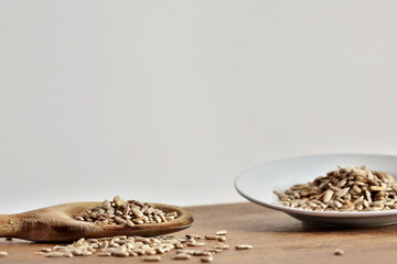 Wooden spoon with portion of shelled sunflower seeds and plate with another portion on the right side out of focus