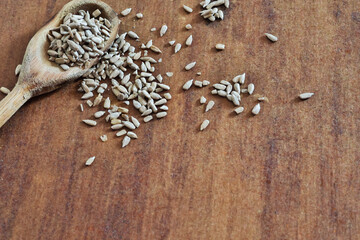 Wooden spoon with portion of shelled sunflower seeds and seeds scattered on the table photographed from above