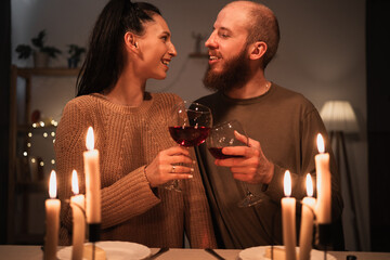 Beautiful young lovely couple having romantic dinner with burning candles and red wine sitting at the table at home