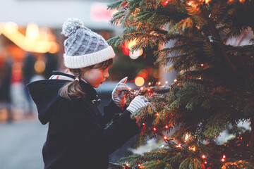 Little cute kid girl having fun on traditional Christmas market during strong snowfall. Happy child...