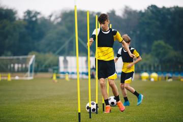 Soccer Players Running With Balls in Between Training Poles. Football Practice Session for Youth Sports Club © matimix