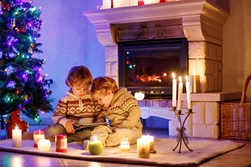 Two cute toddler boys, blond twins playing with new tablet gift. Family celebrating Christmas holiday