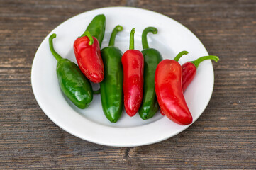 Capsicum annuum Jalapeno chilli hot peppers, group of green and red fruits on wooden brown table on white plate