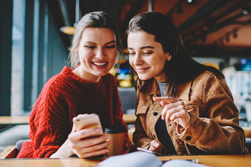Happy caucasian hipster girls reading text message from friend using telephone device for communication, positive women spending free time with technology at college campus in break of studying