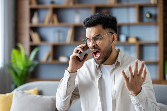 Angry man shouting on phone in modern living room expressing frustration and stress