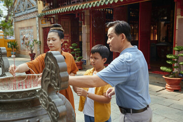 Buddhist family praying with aroma sticks outside the temple © DragonImages
