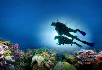 scuba diver diving on tropical reef with blue background and fish