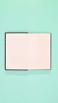 Black hardcover book appear and open on cyan background. Vertical stop motion