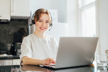 Remote work at home. Woman in headset working on Laptop at Kitchen Table in tiny flat. Student has online classes. Manager has video meeting. Customer support operator in telemarketing service