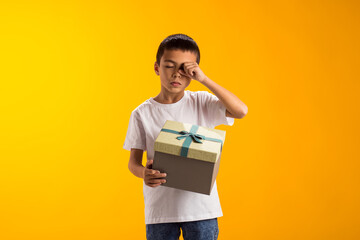 Child boy holding giftbox and crying because he doesn't like the gift. Birthday and celebration concept