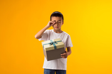 Child boy holding giftbox and crying because he doesn't like the gift. Birthday and celebration concept