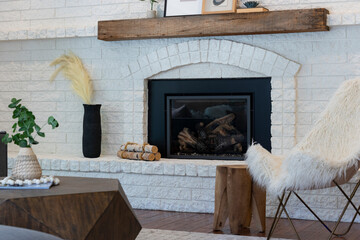 Contemporary living room details of faux fur arm chair and wood coffee table near large white brick fireplace with wooden mantel.