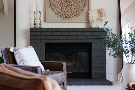 Elegant living room details of leather arm chair near fireplace with darkly painted mantel and decorative items.