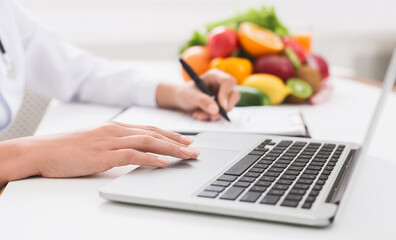 Nutritionist working on laptop and writing diet plan for patient, panorama, copy space