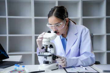 Young researcher in a lab coat and safety glasses conducting research with a microscope in a state of the art laboratory