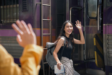 Young woman with a backpack bids farewell to a friend from the train platform, embarking on her journey