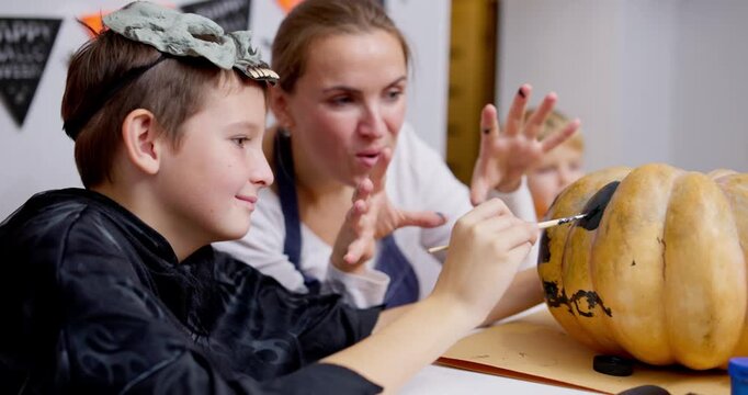 Child in costume painting a pumpkin with his mother