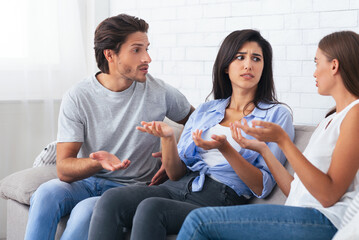 Misunderstanding In Friendship. Three Angry Friends Having Quarrel Arguing Sitting On Sofa At Home. Selective Focus