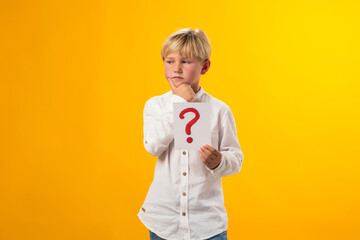 Thoughtful kid boy holding question mark card in hand and touching his chin. Education and curiosity concept