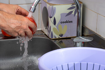 Hands washing fresh tomatoes under the tap.