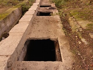 A concrete structure for draining water in the middle of an abandoned industrial workshop.