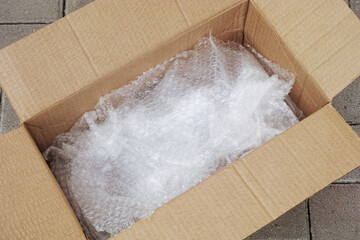 An open cardboard box with bubble wrap inside of it lying on tiles. Close up.