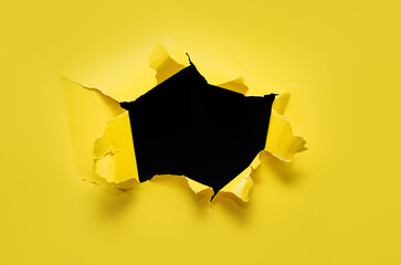 Torn hole in yellow paper with black empty background. Copy space, mockup. Place for text or logo.