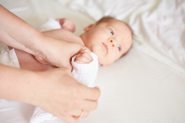 Parent Dressing Newborn Baby in White Onesie on White Bedding