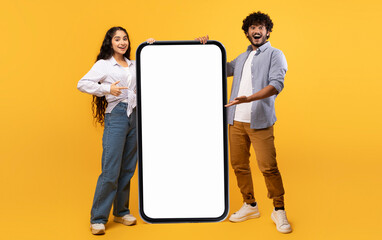 Cool mobile offer. Happy indian couple pointing at big cellphone with white screen for mockup,...