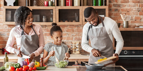 African mom and daughter watching dad while cooking together at home, panorama with copy space