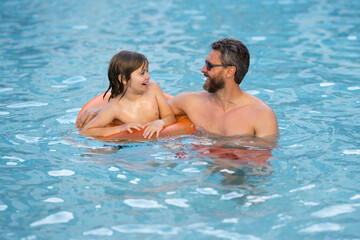 Father and son swimming in pool, summer family weekeng. Father and son splash water in pool on summer family holiday. Dad and child relaxing in pool water. Child with dad swimming in pool.