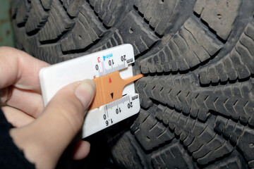 A person is using a ruler to measure the depth of a tire tread