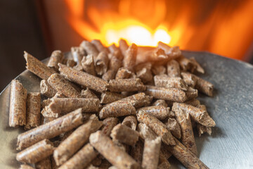wood sawdust pellets for wood stoves, ecological biofuel with fire stove in background. Selective focus