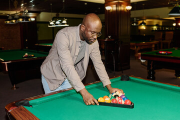 Young bald African American male billiards player bending over wide table and putting triangular...