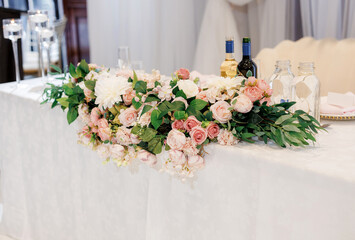 The bride and groom's table decorated with flowers in a restaurant. Table of the bride and groom at a wedding banquet with white and red wine and flower decoration